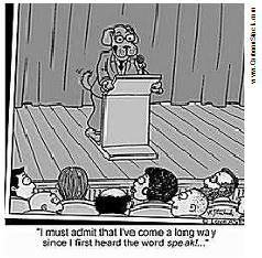 A dog in a businness suit standing behind a lectern in front of an audience. The caption 
                            reads "I must admit that I've come a long way since I first heard the word 'speak'"